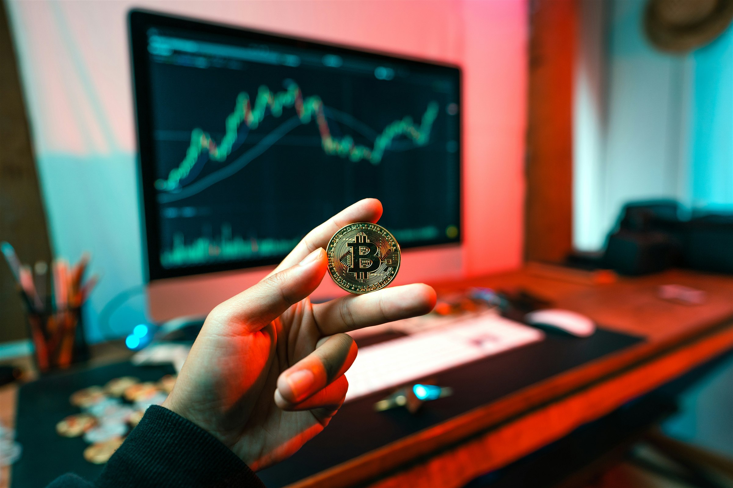 A physical Bitcoin held in front of a rising cryptocurrency price chart